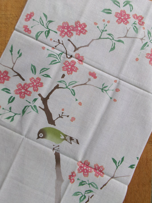 Japanese tenugui towel with cherry blossoms and white-eyes design from Kamawanu, featuring vibrant cherry blossom and bird patterns.